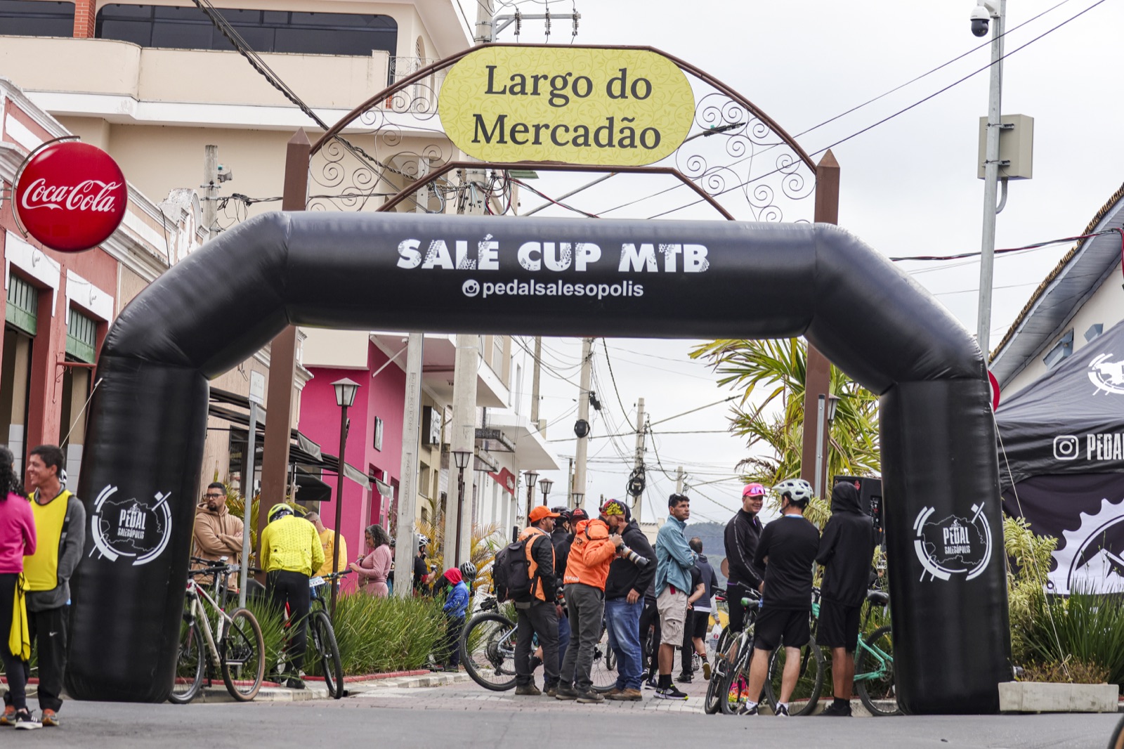 Ciclistas reunidos sob o pórtico da Salé Cup MTB no Largo do Mercadão, em Salesópolis.
